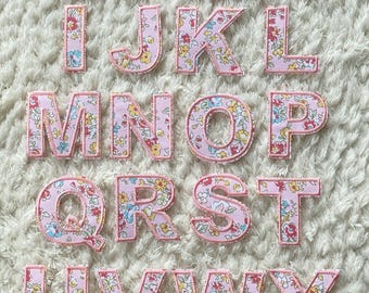 Könnte beinhalten: Ein Satz von 26 pinkfarbenen Stoffbuchstaben mit Blumenmuster. Jeder Buchstabe ist mit einem dunkleren Pink umrandet.