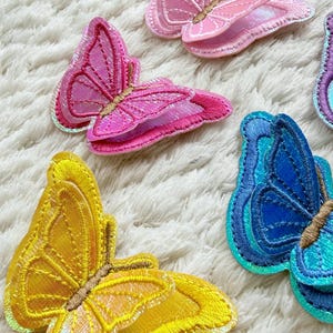 May include: Embroidered butterfly patches in shades of pink, yellow, and blue. The patches have iridescent accents and detailed stitching. These decorative butterfly patches are suitable for clothing, accessories, or craft projects.