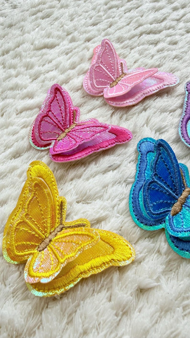 May include: Embroidered butterfly patches in shades of pink, yellow, and blue. The patches have iridescent accents and detailed stitching. These decorative butterfly patches are suitable for clothing, accessories, or craft projects.