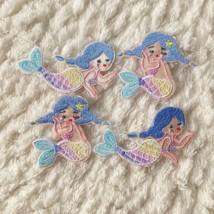 Può includere: Quattro toppe ricamate da stirare raffiguranti sirene con capelli blu e code colorate. Le sirene sono in varie pose, tra cui sedute, nuotando e tenendo una conchiglia.