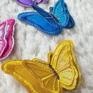 May include: Embroidered butterfly patches in various colors, including yellow, blue, purple, and pink. The patches have detailed stitching and are likely for decorative purposes, such as embellishing clothing or accessories.