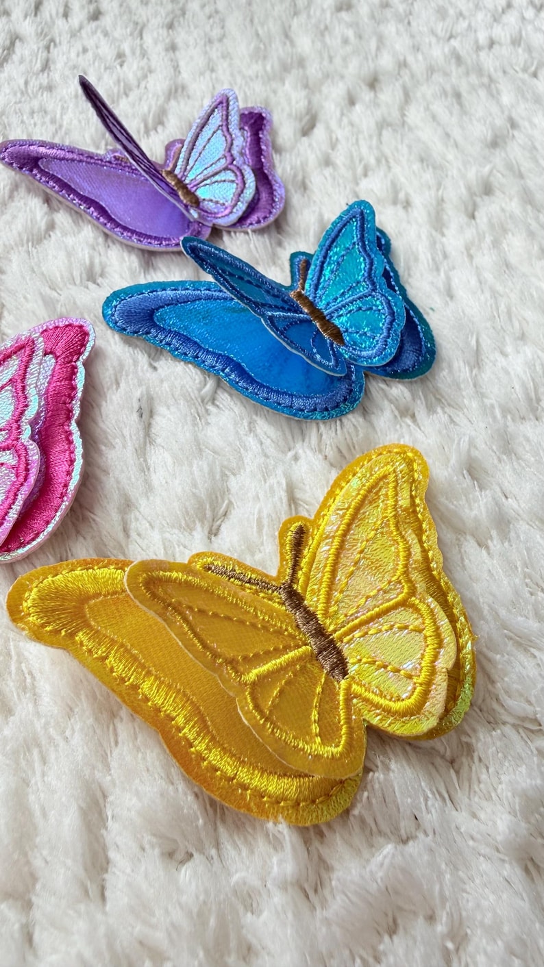 May include: Embroidered butterfly patches in various colors, including yellow, blue, purple, and pink. The patches have detailed stitching and are likely for decorative purposes, such as embellishing clothing or accessories.