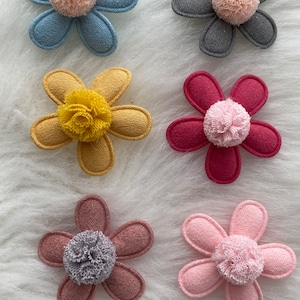 Puede incluir: Seis pinzas para el pelo de flores de fieltro con centros de pompón. Las flores son en tonos de azul, gris, amarillo, rosa, rojo y marrón.