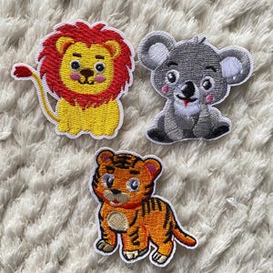 May include: Three embroidered iron-on patches featuring cartoon animals: a red-haired lion, a gray koala, and an orange tiger.