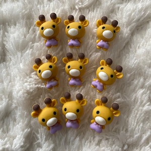 Pode incluir: Dez figuras de girafa amarelas e marrons com roupas roxas. As figuras são feitas de um material macio e flexível.