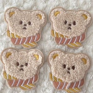 May include: Four beige fuzzy bear appliques with brown eyes and a pink and yellow striped scarf. The bears are embroidered with a fuzzy texture.