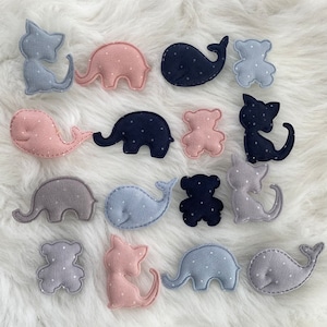 May include: A set of 15 felt appliques featuring various animals and shapes, including whales, elephants, cats, bears, and a few abstract shapes. The appliques are all in shades of pink, blue, and grey with white polka dots.