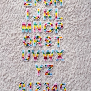 May include: Rainbow-colored alphabet letters and numbers arranged on a white, textured surface. The letters A through Z and numbers 0 through 9 are displayed, each with a vibrant, striped design in multiple colors.