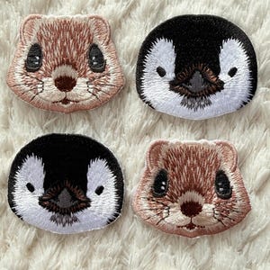 May include: Four embroidered patches featuring animal faces: two penguins and two weasels. The penguin patches are black and white, while the weasel patches are brown and tan. The patches are on a white, textured background.
