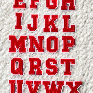 Op de afbeelding: Rode vilt letter patches met witte contouren, met het volledige alfabet van A tot Z.