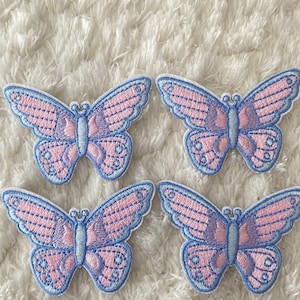 May include: Four pink and blue butterfly iron-on patches. The butterflies have a light pink and purple striped pattern with a blue outline.