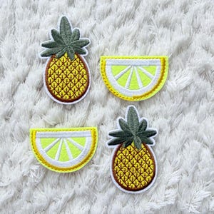 May include: Four embroidered patches: two pineapples and two lemon slices. The pineapples are yellow with brown outlines and green tops. The lemon slices are yellow with white and yellow outlines.