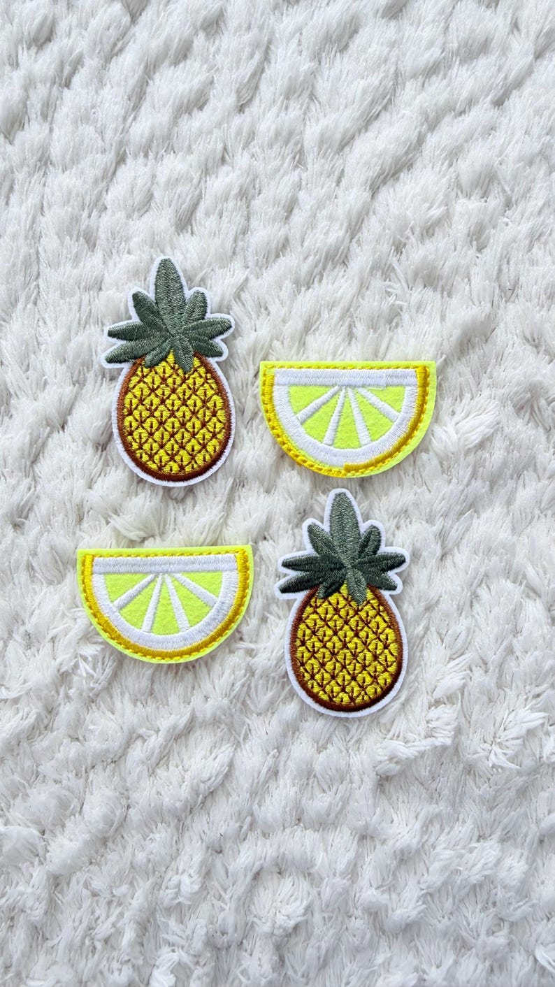 May include: Four embroidered patches: two pineapples and two lemon slices. The pineapples are yellow with brown outlines and green tops. The lemon slices are yellow with white and yellow outlines.