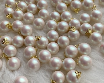 May include: A large group of white pearl buttons with gold loop closures. The buttons are scattered on a white fluffy surface.