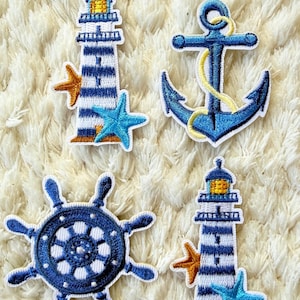 May include: Four nautical-themed embroidered patches. Designs include a blue and white striped lighthouse, a blue anchor with yellow rope, a blue ship's wheel, and a starfish. The patches are on a white, textured background.