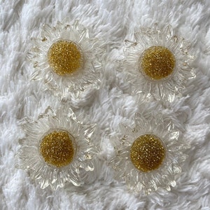 Puede incluir: Cuatro adornos de plástico transparente en forma de girasol con centros de purpurina dorada.