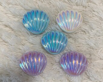 May include: Five iridescent seashell-shaped trinket boxes in various shades of blue and white. The boxes are made of a smooth, shiny material and have a slightly raised design.
