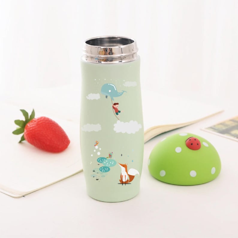 May include: A green stainless steel water bottle with a whimsical design featuring a fox, a boy, and a whale. The bottle has a green lid with a ladybug on top.