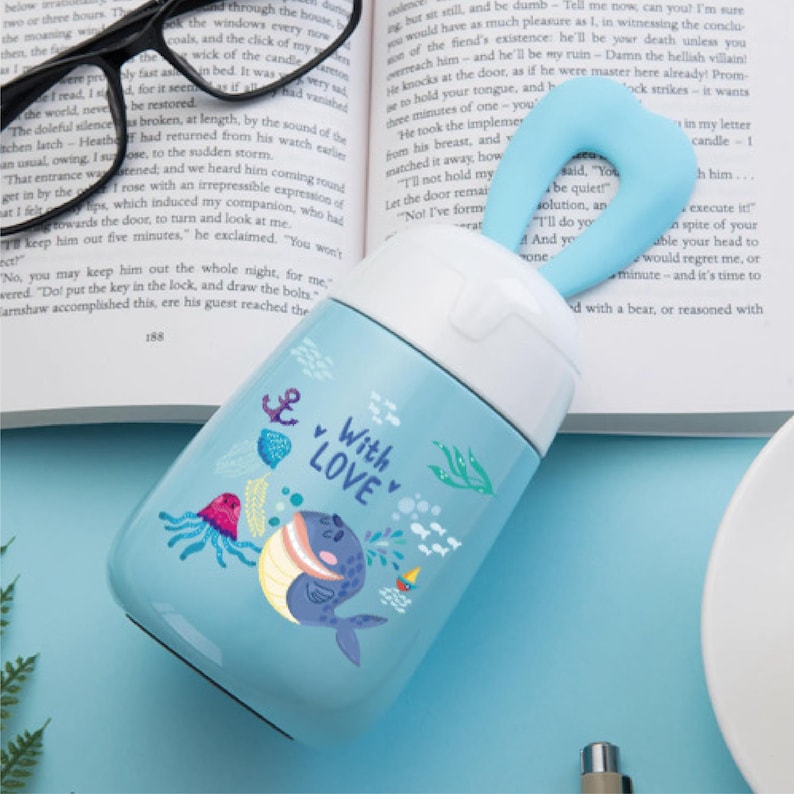May include: A light blue stainless steel water bottle with a white lid and a blue silicone handle. The bottle features a cartoon whale design with the words "With Love" on it.