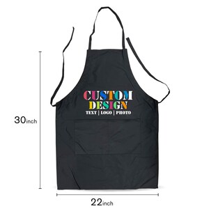 May include: Black apron with a large pocket and adjustable straps. The apron has the text "CUSTOM DESIGN TEXT | LOGO | PHOTO" printed on the front in colorful letters.