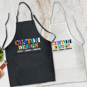 May include: Two aprons, one black and one white, with the text "CUSTOM DESIGN TEXT | LOGO | PHOTO" printed in colorful letters.