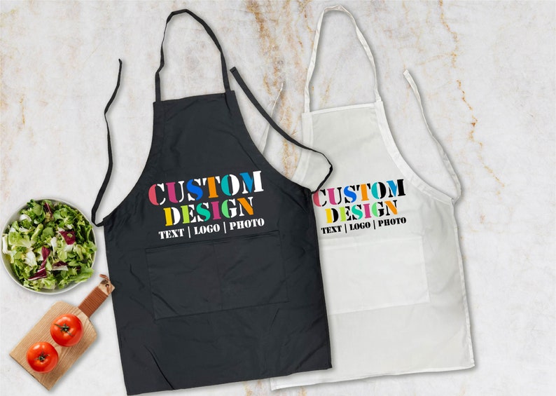May include: Two aprons, one black and one white, with the text "CUSTOM DESIGN TEXT | LOGO | PHOTO" printed in colorful letters.