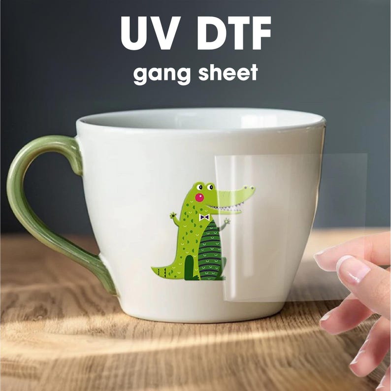 May include: A white ceramic mug with a green handle, featuring a green alligator with a red bow tie and green and white stripes. The alligator is printed on a clear sheet that is being peeled off the mug. The text "UV DTF gang sheet" is printed above the mug.