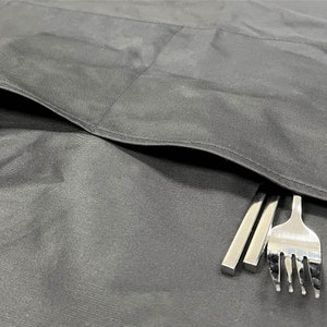 May include: A black fabric apron with a large pocket on the front. Two silver chopsticks and a silver fork are sticking out of the pocket.