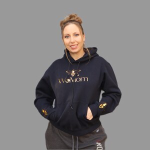May include: Black hooded sweatshirt with a gold bee and the text "WoMom" on the front. The sleeves have a gold bee design.