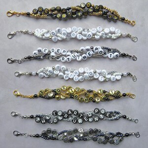 May include: A collection of beaded bracelets, each spelling out words with letter beads. The bracelets use gold, silver, black, and white beads. Phrases include "THE DEPT OF ARTS", "THE DEPT OF POETS", and other text.