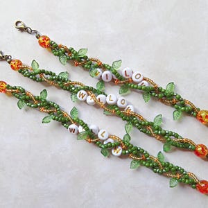 May include: Three beaded bracelets with the name "WILLOW" spelled out in white letter beads. The bracelets feature green beads, gold accents, and small green leaf charms. Each bracelet has a decorative clasp.