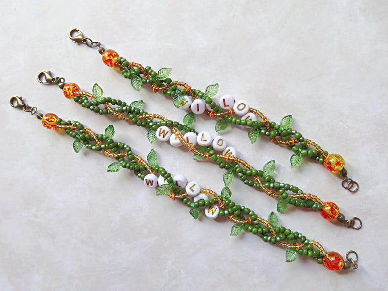 May include: Three beaded bracelets with the name "WILLOW" spelled out in white letter beads. The bracelets feature green beads, gold accents, and small green leaf charms. Each bracelet has a decorative clasp.