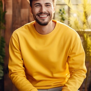 May include: A man wearing a yellow sweatshirt and grey trousers smiles at the camera.