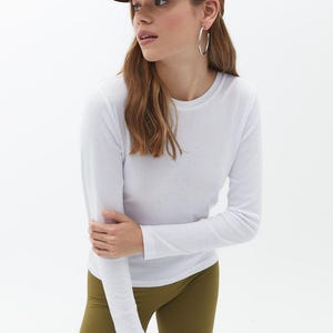 May include: A white long-sleeved t-shirt with a brown baseball cap that says "easy" on it. The person is wearing olive green leggings.
