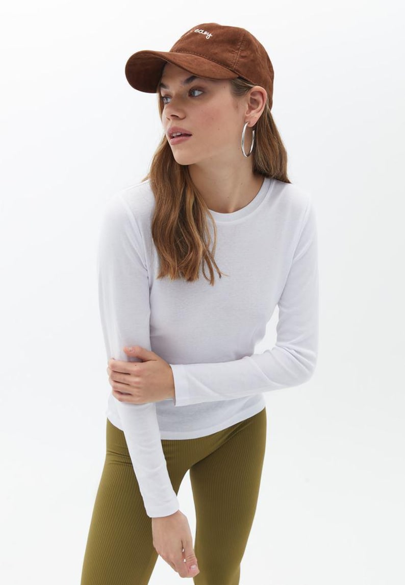 May include: A white long-sleeved t-shirt with a brown baseball cap that says "easy" on it. The person is wearing olive green leggings.