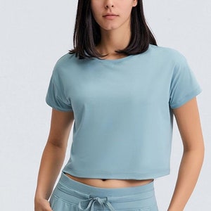 K&ouml;nnte beinhalten: Ein hellblaues Crop-Top und eine passende Jogginghose. Das kurz&auml;rmelige Oberteil hat einen Rundhalsausschnitt und einen verk&uuml;rzten Saum. Die Jogginghose hat einen Kordelzug in der Taille und Taschen. Das Model tr&auml;gt das Sportbekleidungsset.