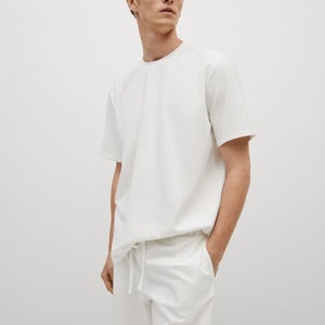 Puede incluir: Una camiseta blanca de manga corta y pantalones cortos blancos con cord&oacute;n. La camiseta tiene un corte holgado y los pantalones cortos tienen un estilo casual.