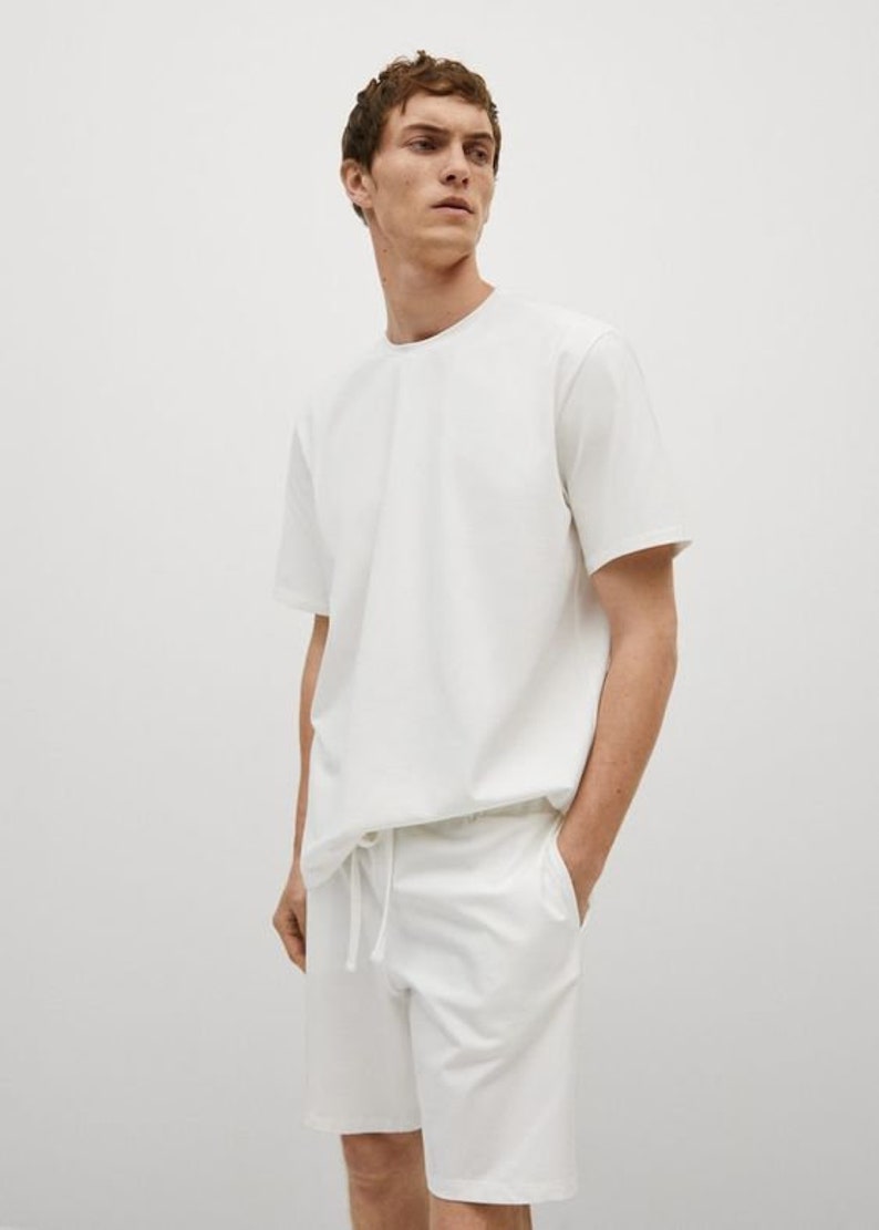 Puede incluir: Una camiseta blanca de manga corta y pantalones cortos blancos con cord&oacute;n. La camiseta tiene un corte holgado y los pantalones cortos tienen un estilo casual.