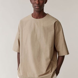 May include: A beige short-sleeved t-shirt with a round neckline. The t-shirt is made from a lightweight fabric and has a relaxed fit.