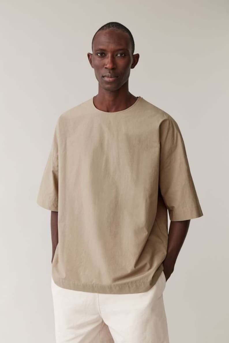 May include: A beige short-sleeved t-shirt with a round neckline. The t-shirt is made from a lightweight fabric and has a relaxed fit.
