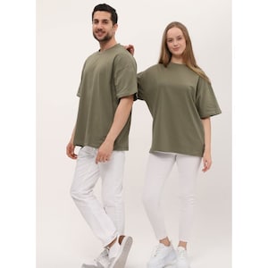 Puede incluir: Dos personas con camisetas de color verde oliva de gran tama&ntilde;o. La persona de la izquierda lleva pantalones blancos y zapatillas blancas. La persona de la derecha lleva pantalones blancos y zapatillas blancas.