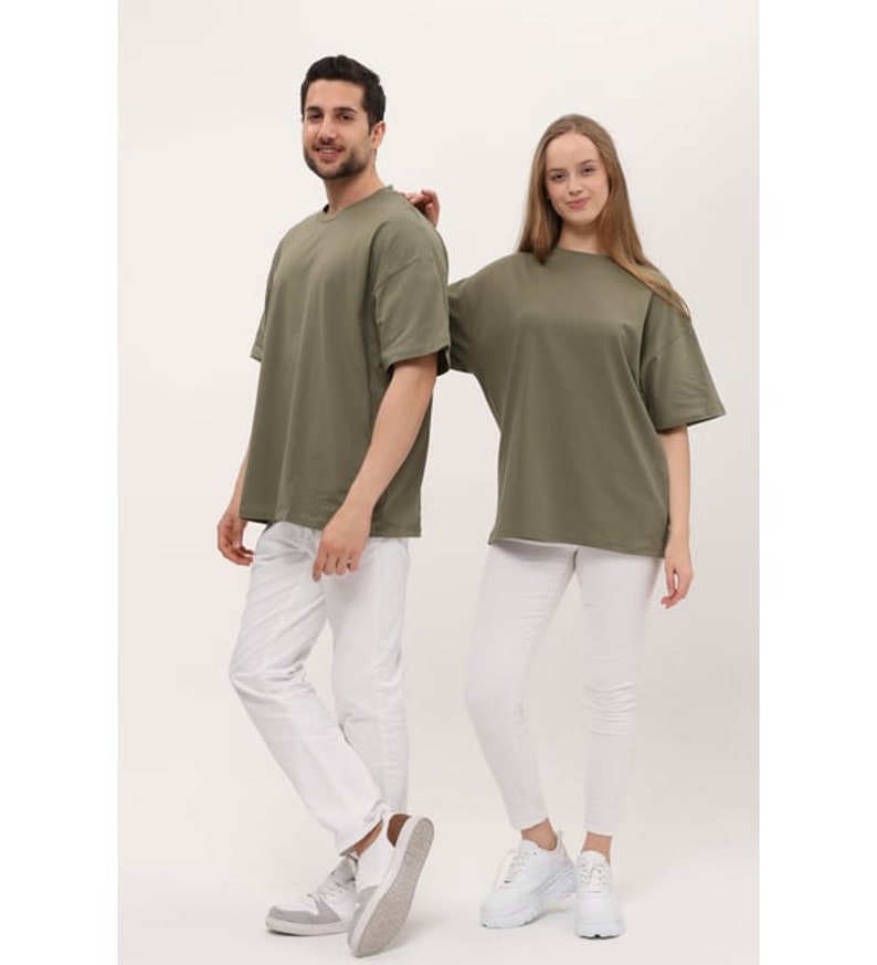 Puede incluir: Dos personas con camisetas de color verde oliva de gran tama&ntilde;o. La persona de la izquierda lleva pantalones blancos y zapatillas blancas. La persona de la derecha lleva pantalones blancos y zapatillas blancas.