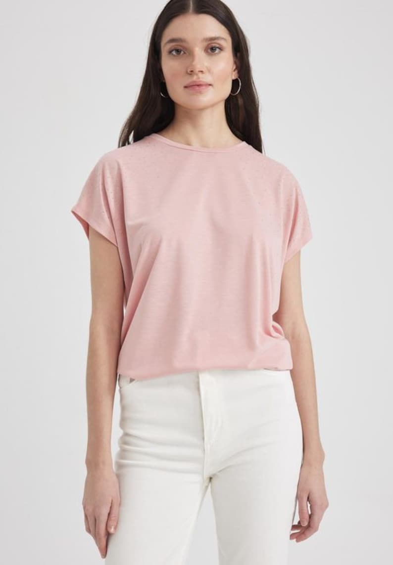 K&ouml;nnte beinhalten: Ein rosa T-Shirt mit kurzen &Auml;rmeln und einem dezenten Glitzereffekt. Das Shirt hat eine lockere Passform und einen runden Ausschnitt.
