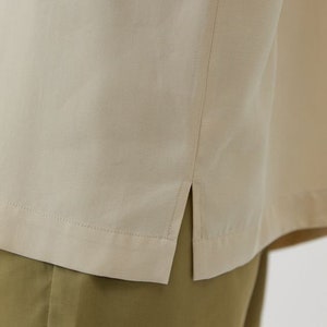 May include: A beige shirt with a side seam detail. The shirt is made of a soft, lightweight fabric and has a relaxed fit.