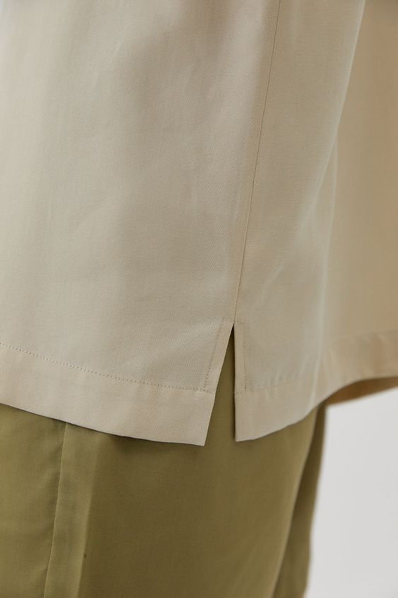 May include: A beige shirt with a side seam detail. The shirt is made of a soft, lightweight fabric and has a relaxed fit.