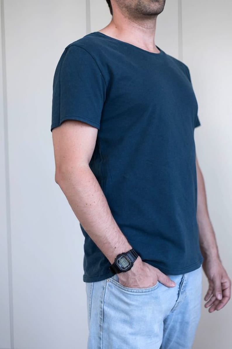 May include: A man wearing a dark blue t-shirt and light blue jeans. He is wearing a black digital watch on his left wrist.