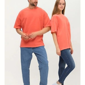 Puede incluir: Dos personas con camisetas de color coral de manga corta y pantalones vaqueros azules. La persona de la izquierda lleva zapatillas blancas. La persona de la derecha lleva zapatillas blancas con plataforma.