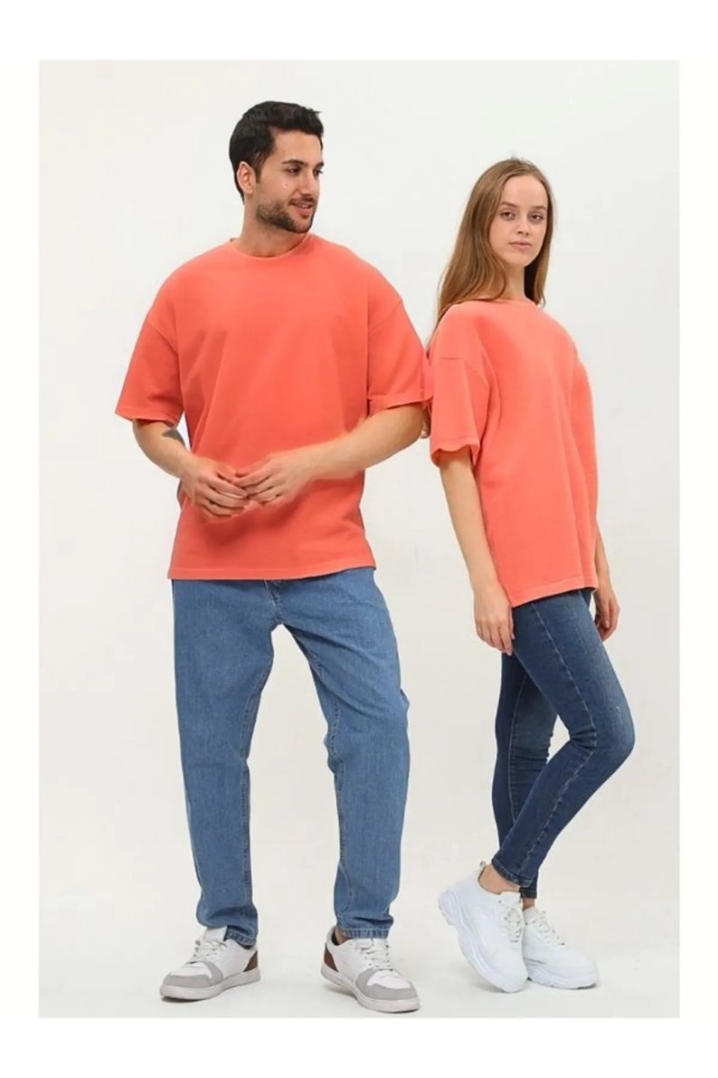 Puede incluir: Dos personas con camisetas de color coral de manga corta y pantalones vaqueros azules. La persona de la izquierda lleva zapatillas blancas. La persona de la derecha lleva zapatillas blancas con plataforma.