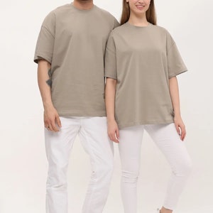 Puede incluir: Dos personas con camisetas de color marr&oacute;n claro de gran tama&ntilde;o y pantalones y zapatos blancos. Las camisetas tienen cuello redondo y mangas cortas.