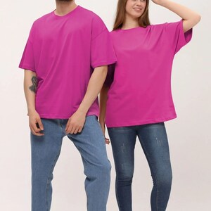 Puede incluir: Dos personas con camisetas rosas de gran tama&ntilde;o a juego y pantalones vaqueros azules. Ambos llevan zapatillas blancas.